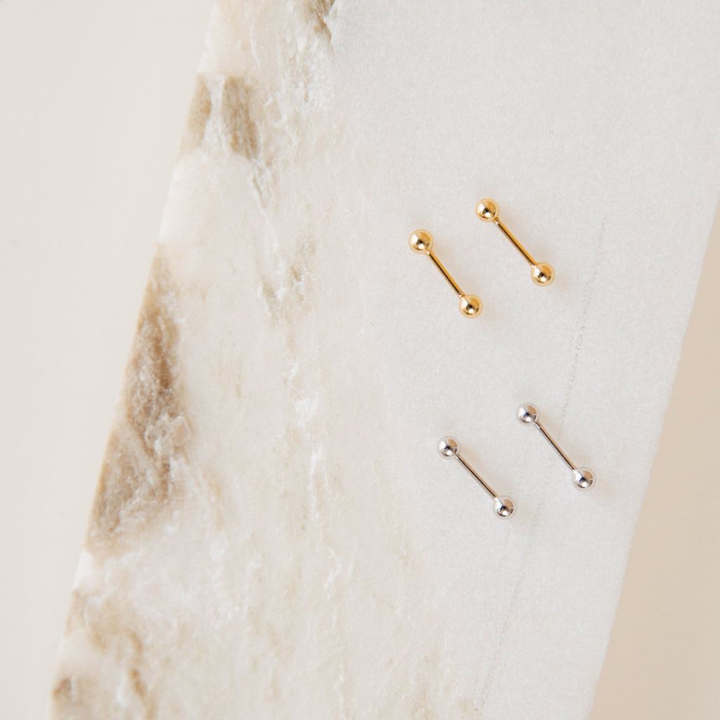The Nora Duo Studs in Sterling Silver—featuring two gold and two silver ball studs—are displayed on textured white marble, making them the perfect classic earrings for your everyday style.