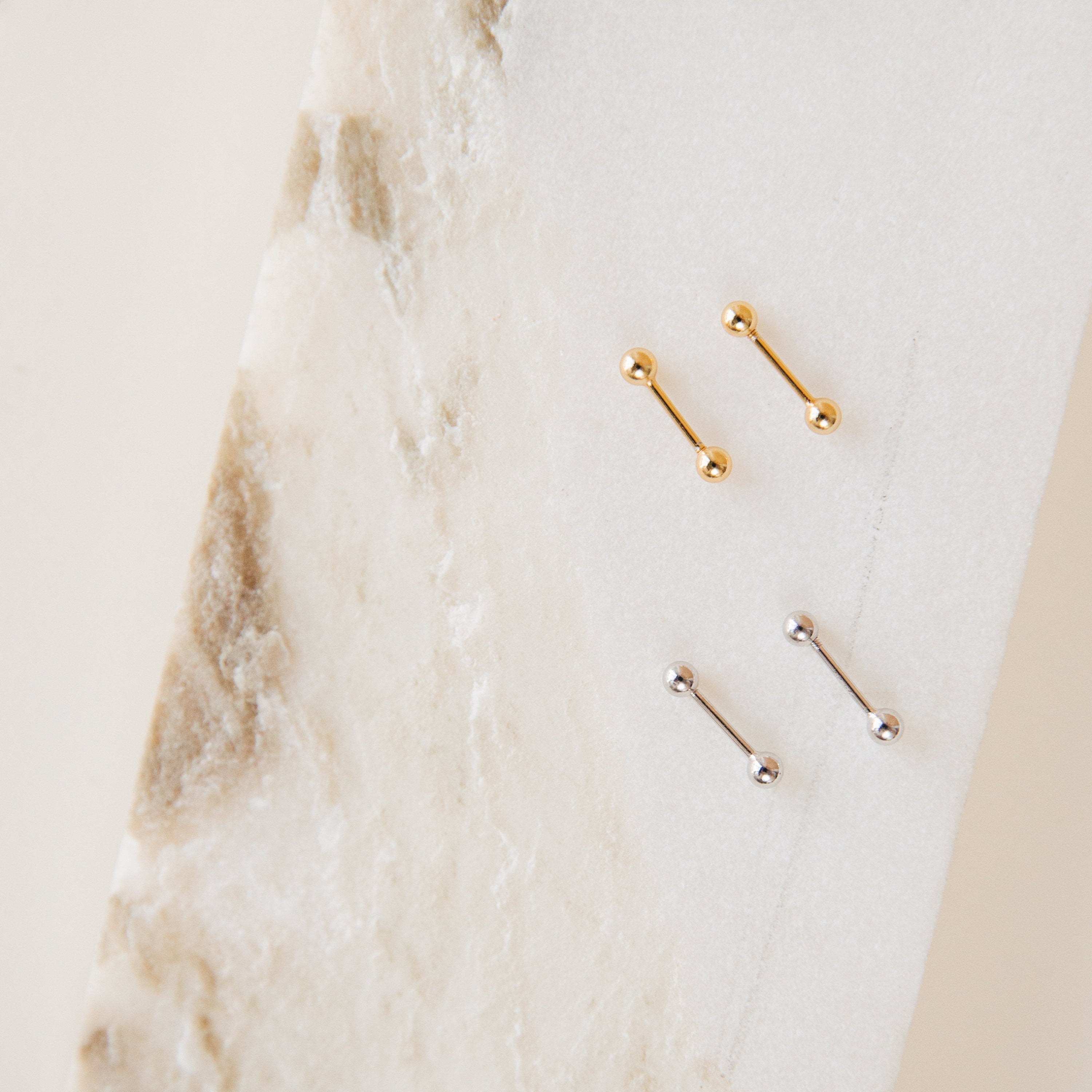 The Nora Duo Studs in Sterling Silver—featuring two gold and two silver ball studs—are displayed on textured white marble, making them the perfect classic earrings for your everyday style.