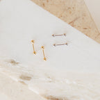 The Nora Duo Studs in Sterling Silver feature two pairs of classic ball stud earrings, one in gold tone and one in silver, displayed on a white marble surface—perfect for effortless, everyday style.