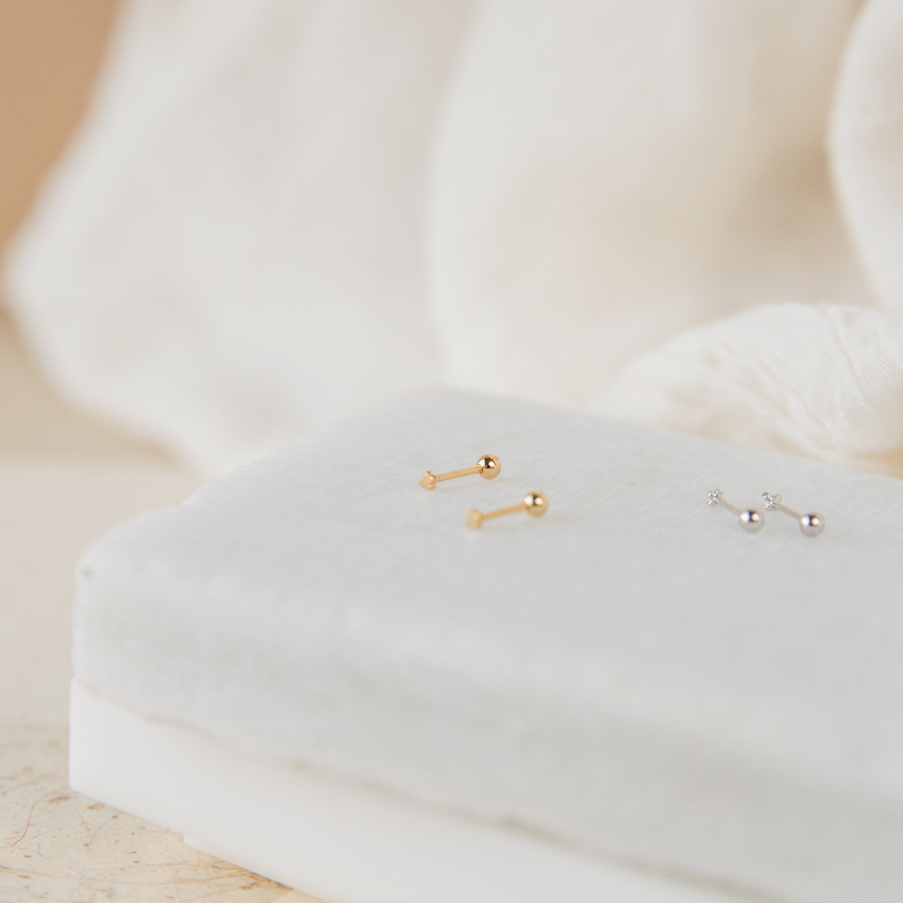 Tiny Cross Studs in gold and silver, displayed on a white, velvet-covered jewelry stand.
