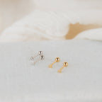 Two pairs of Tiny Heart Studs—one silver, one gold—are shown on a light textured surface. These earrings are perfect for everyday wear and make a thoughtful gift for someone special.
