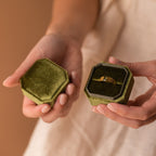 Hands holding an open green velvet ring box with the Olive Peridot Signet Ring inside, against a warm background.