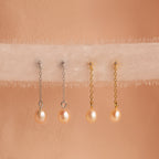 Two pairs of Isha Pink Pearl Earrings—one with silver dangling chains and one with gold—are displayed on soft fabric.