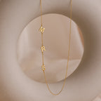 The Sideways Initial Necklace is shown with dangling letters spelling MRS on a round, beige abstract background—a unique and thoughtful Christmas gift.