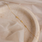 Sideways Initial Necklace with M, R, and S letter charms shown on a marble tray with sheer fabric—a unique piece that's perfect for Christmas gifting.