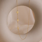 The Venice Sideways Initial Necklace showcases gold letters M, R, and S on a soft beige circular background, offering an elegant twist on personalized initial jewelry.