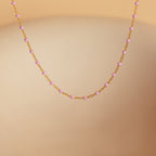 The Pink Station Necklace features a dainty gold chain with small pink beads, shown against a soft beige background. Perfect as a delicate accessory for any occasion.