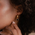 A close-up of a person wearing the Onyx Diamond Earrings Set, featuring gold hoops with black oval pendants, gently touching their chin.
