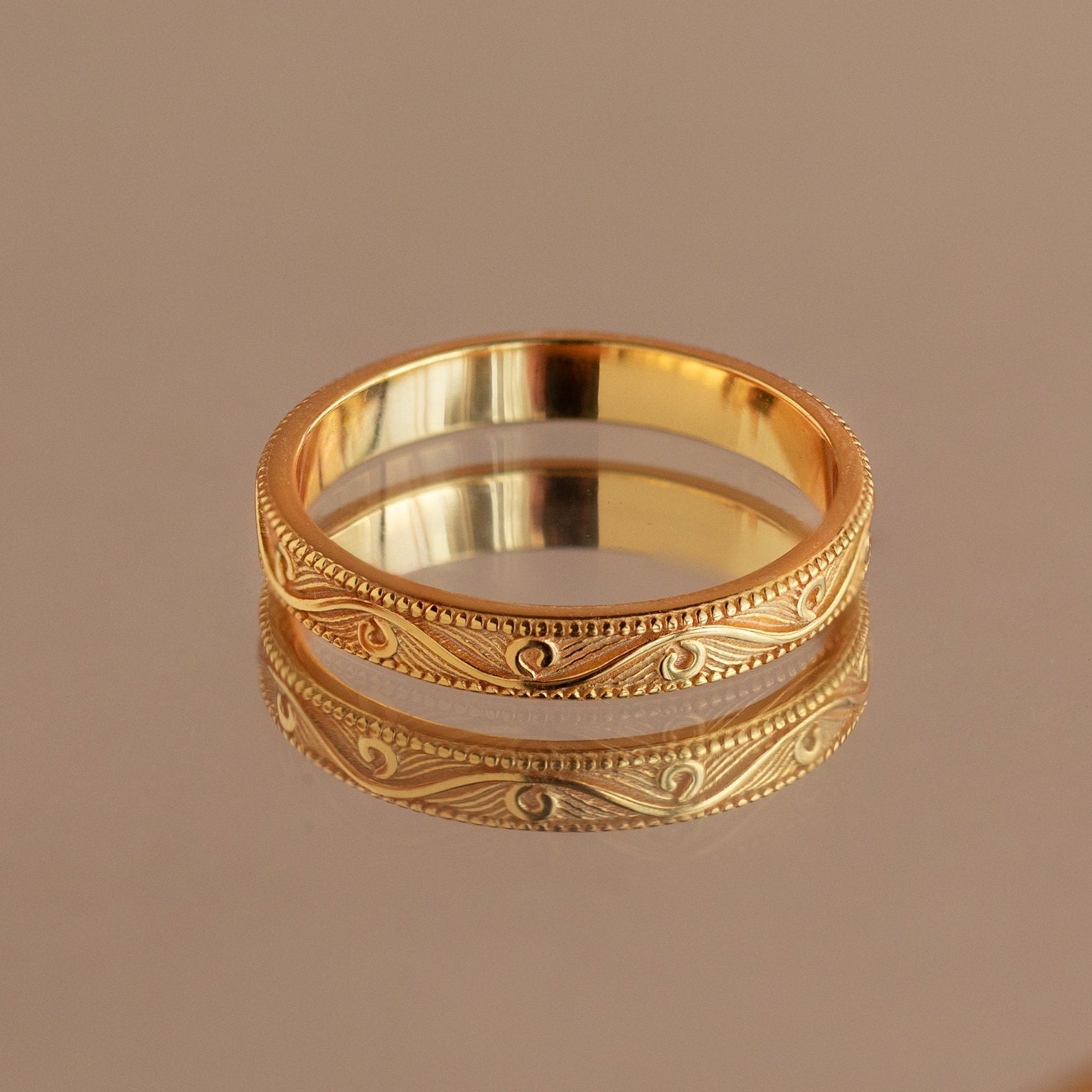 Gold filigree ring with intricate pattern, reflected on a polished mirror surface.