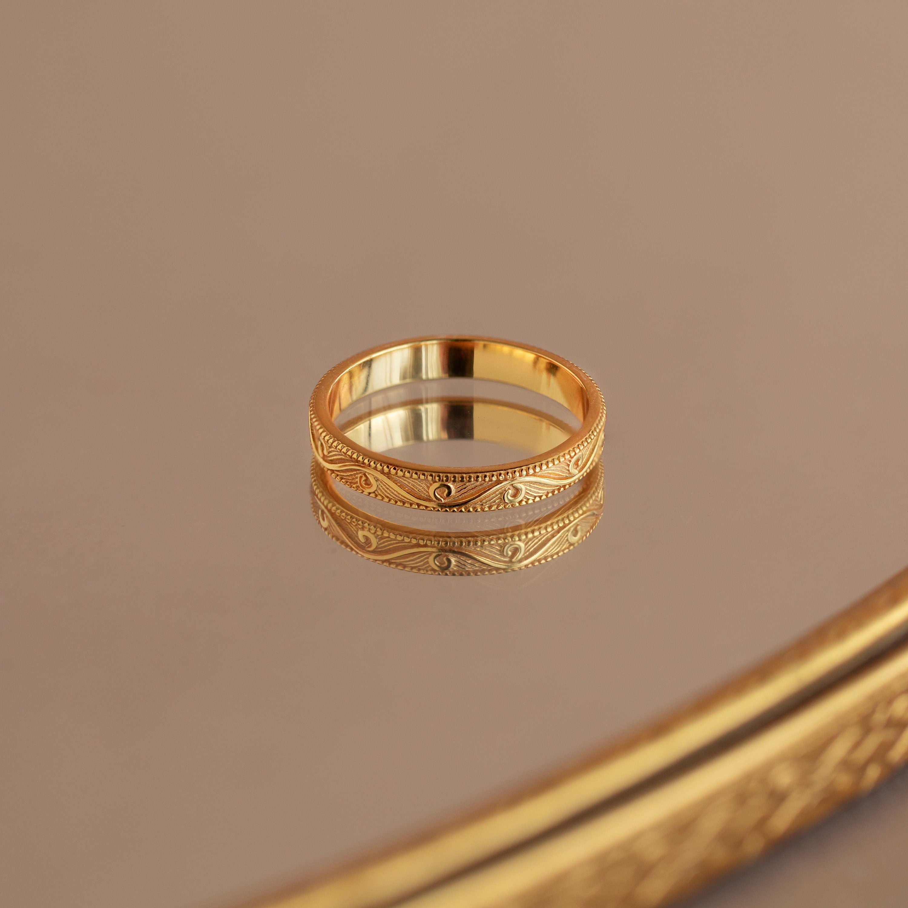 Gold filigree ring with intricate pattern, reflected on a polished mirror surface.