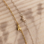 Gold and silver chain bracelets with letter A charms rest on a textured beige surface—perfect for stacking with your favorite initial jewelry or pairing with the Venice Sideways Initial Necklace.