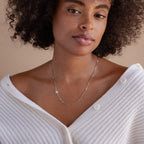 Woman with curly hair wears a white sweater and the Birthstone Initial Necklace in Box Chain, personalized with an M pendant.