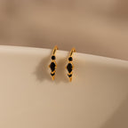 The Amaya Black Marquise Threaders, featuring gold hoops with black gemstone accents, rest on a smooth cream-colored surface—a stunning addition to any modern earrings collection.
