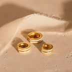 Three White Opal Inlay Huggies are displayed on a light textured surface next to beige fabric.