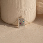 The Calendar Birthstone Necklace features a personalized calendar pendant with highlighted dates, displayed before a textured ceramic vase—a unique and meaningful gift.