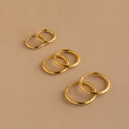 The Mini Bold Hoops Set—three pairs of classic hoops in small, medium, and large—are arranged on a beige surface.