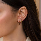 Close-up of a woman's ear with two Mini Hammered Hoops and long brown hair, highlighting the elegance of these gold or silver hoop earrings.
