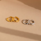 The Mini Hammered Hoops Set features gold and silver hammered hoop earrings displayed on a beige surface, offering classic hoops in both finishes perfect for any occasion.