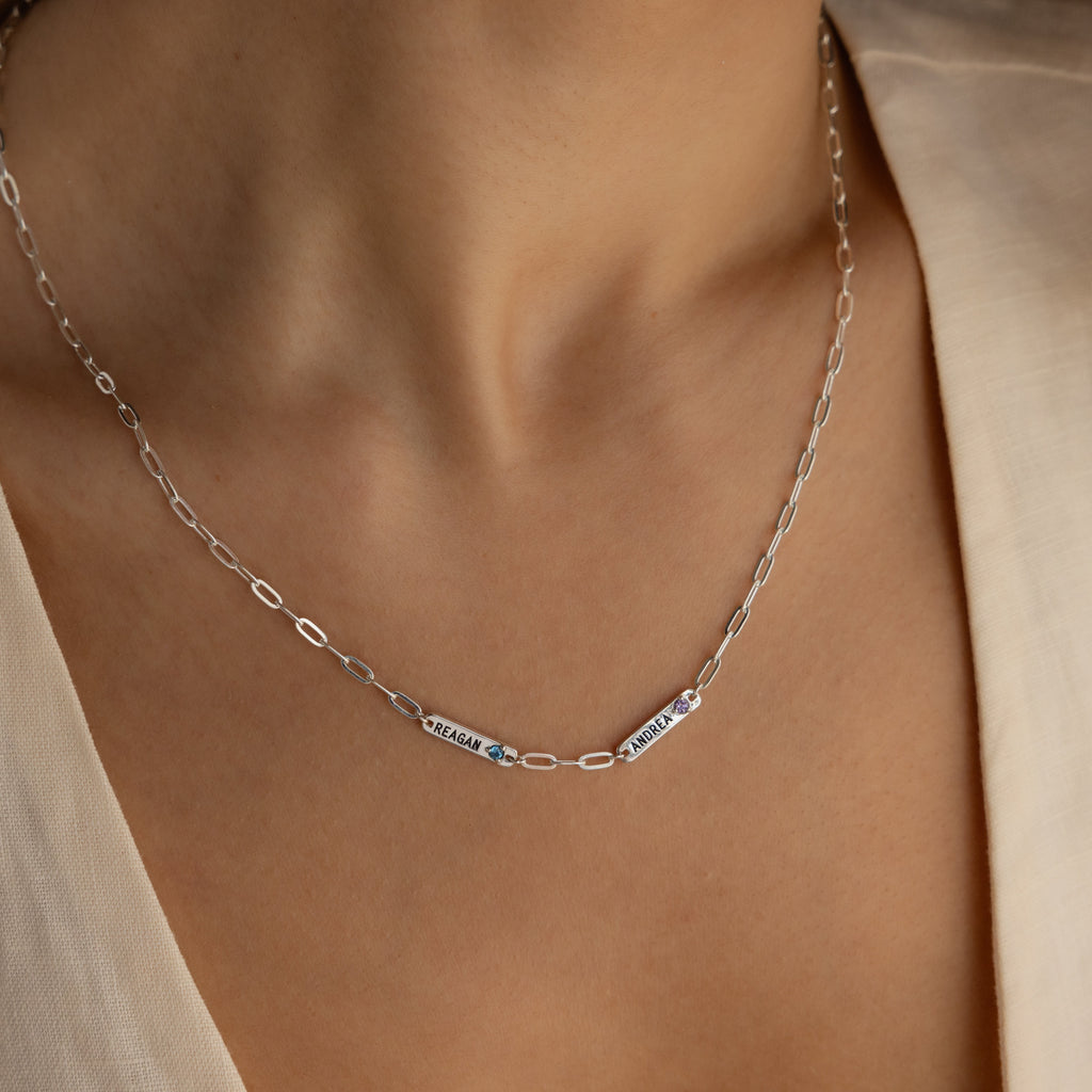 The Mini Name Birthstone Necklace features two personalized bar nameplates reading SERGAM and ZULYA, elegantly worn on a woman's neck—a unique customized gift.
