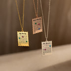 The Calendar Birthstone Necklace features gold and silver chains, each personalized with colorful birthstones and engraved family names—a unique piece of customized jewelry.