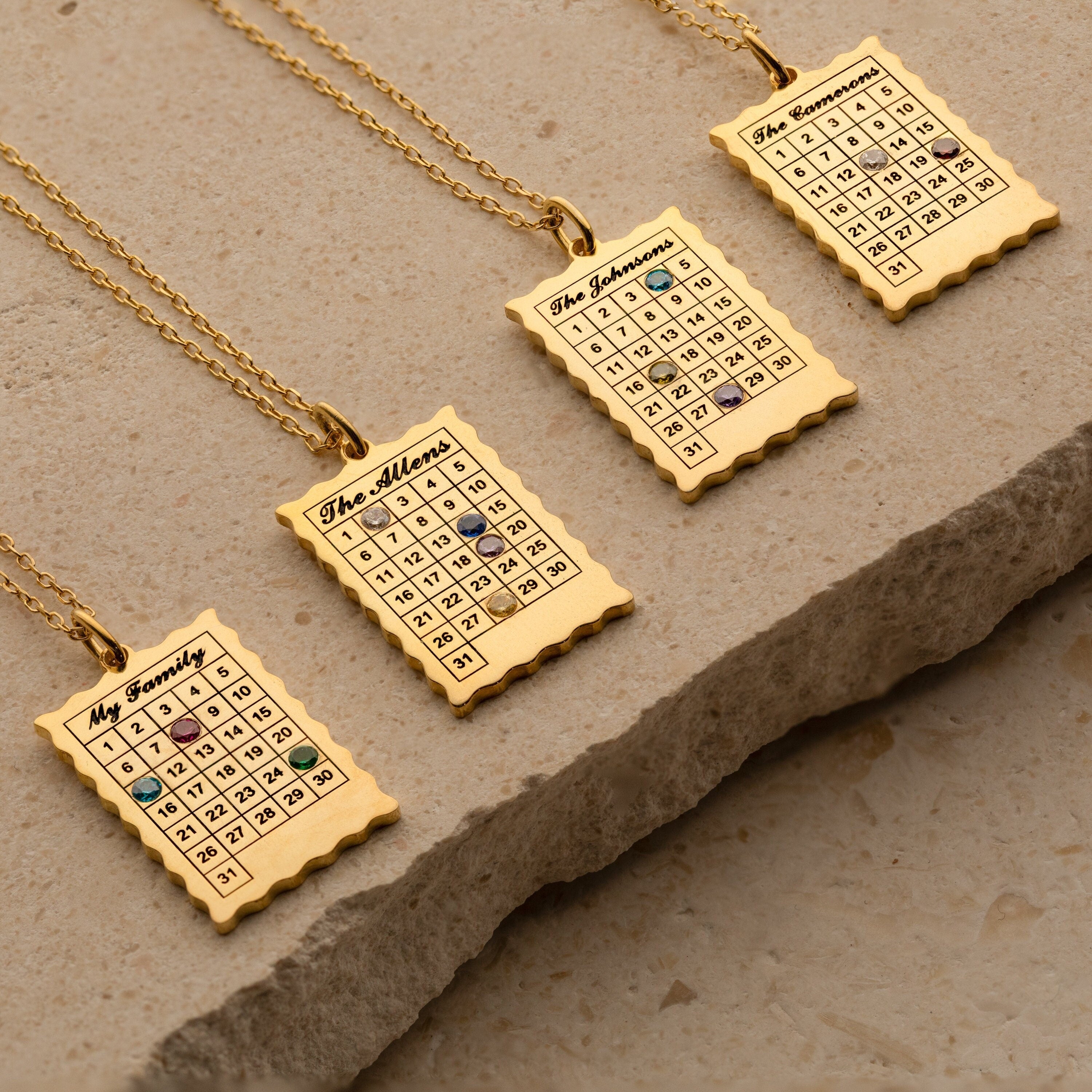 Four gold Calendar Birthstone Necklaces on chains, each personalized with a name and date marked by a birthstone gem—unique keepsake jewelry for any occasion.