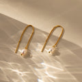 Pearl Threader Earrings are shown on a neutral background, their minimalistic gold design and pearls highlighted by soft, reflective lighting.