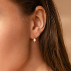 Close-up of a woman's ear wearing Dainty Knot Pearl Earrings in 18K Gold—featuring a delicate gold knot with a single white pearl—for a look of classic charm and timeless sophistication.