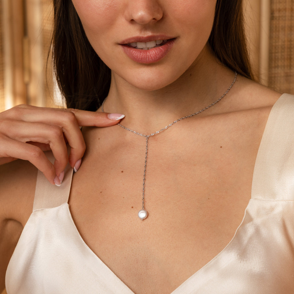 A woman wearing a cream dress and the Pearl Lariat Y Necklace with a delicate pearl charm, achieving an effortlessly elegant look.