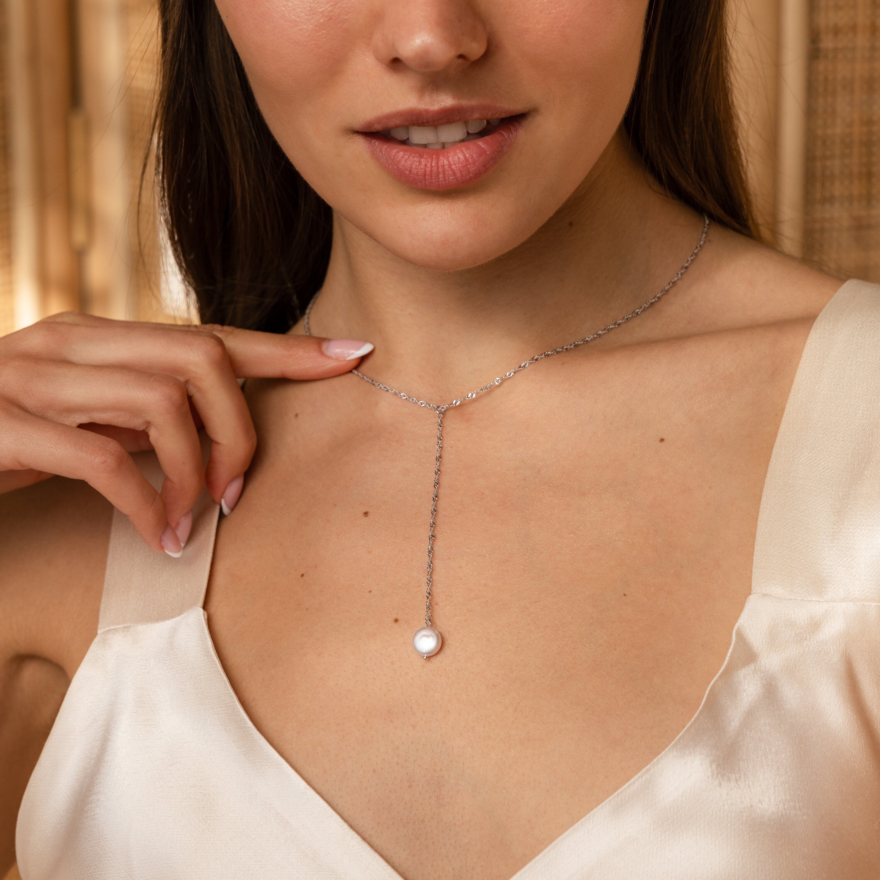 A woman wearing a cream dress and the Pearl Lariat Y Necklace with a delicate pearl charm, achieving an effortlessly elegant look.