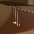 Two pairs of Pearl Threader Earrings—one in gold, one in silver—are elegantly displayed, hanging from the edge of a surface.