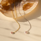 Two pearl necklaces—a gold dainty chain and the Pearl Lariat Y Necklace in silver—are displayed on a shell against a beige background.
