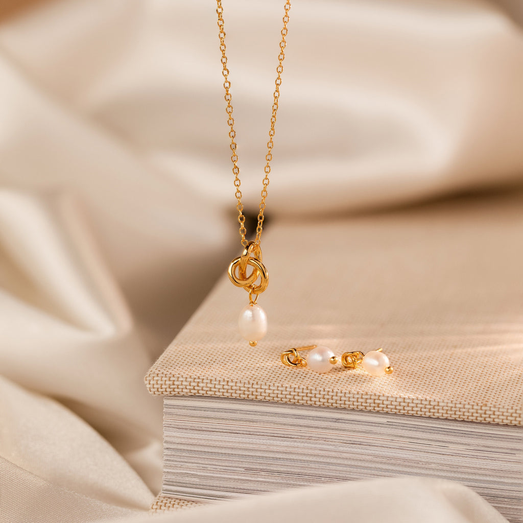 Dainty Knot Pearl Necklace displayed on a closed book with a backdrop of soft beige fabric.