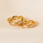 A pair of Marquise Inlay Huggies with sparkling clear stones is displayed on a soft, cream-colored fabric background.
