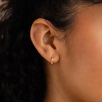 Close-up of a woman's ear wearing a small gold hoop earring with three sparkling stones, perfect for layering or pairing with the Diamond Butterfly Earrings Set.