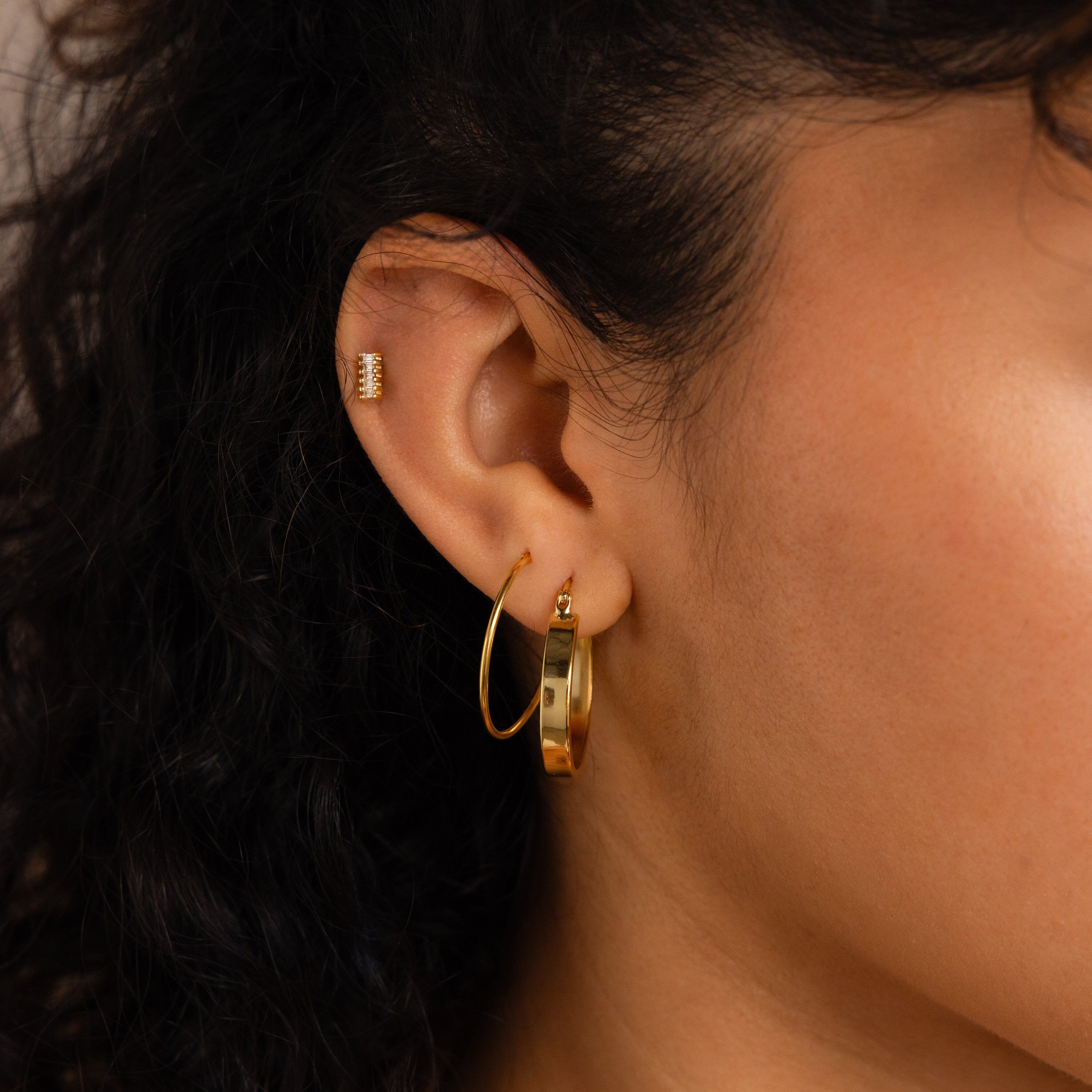 A close-up of a woman's ear adorned with Thick Hoops.