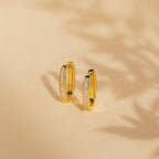 Baguette Link Hoops: minimalist geometric gold earrings with embedded white stones, displayed on a beige surface with soft shadows.