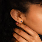 A woman's hand gently touches her neck, showcasing the Sapphire Diamond Drop Earrings on her ear.