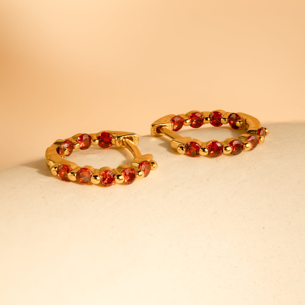 Inside Out Garnet Huggies: gold hoop earrings featuring small red gemstones, perfect as stylish garnet huggies or gemstone earrings, shown on a neutral beige surface with a soft background.