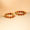 Inside Out Garnet Huggies: gold hoop earrings featuring small red gemstones, perfect as stylish garnet huggies or gemstone earrings, shown on a neutral beige surface with a soft background.