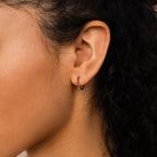 Close-up of a woman's ear adorned with Inside Out Garnet Huggies, highlighted by dark curly hair and smooth skin.