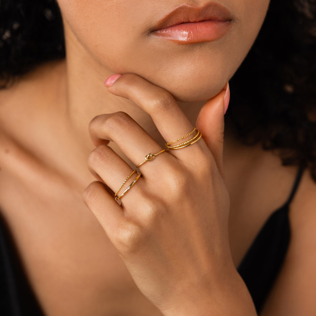 A woman with soft makeup wears the Textured Stacking Ring Set, resting her chin on her hand in a black top.