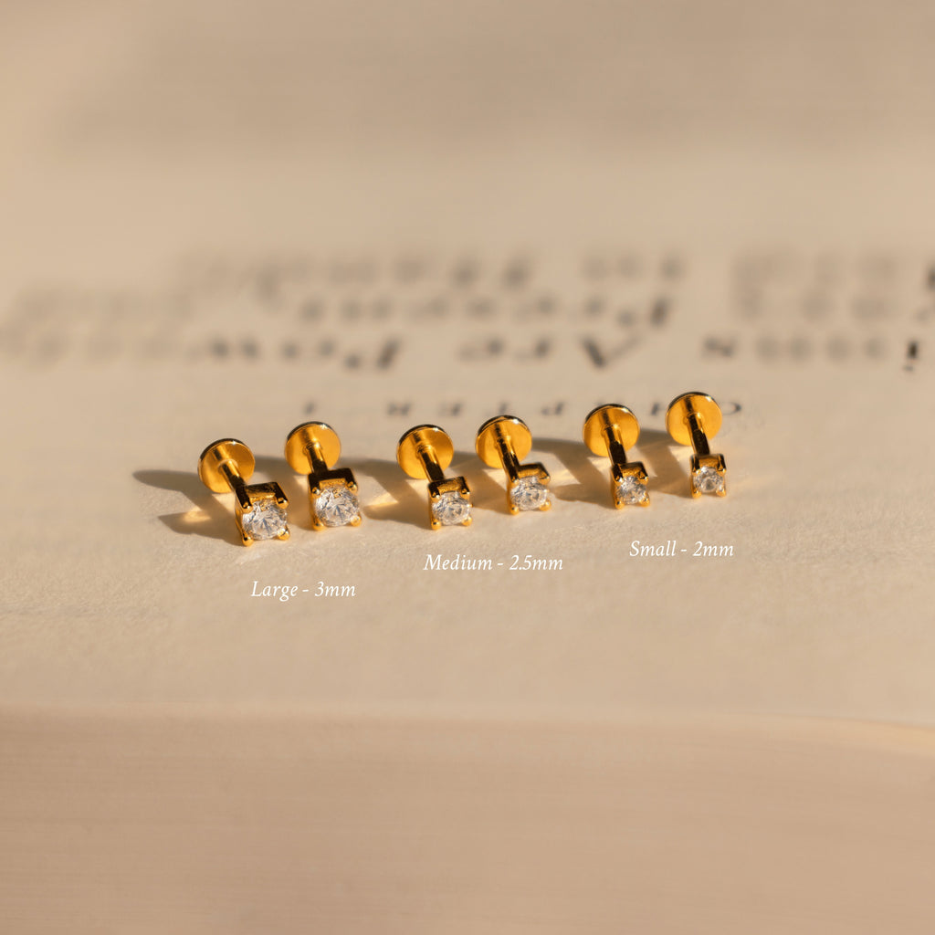 Three pairs of Diamond Flatback Studs Set in 18K Gold, in large, medium, and small sizes, are beautifully displayed on a beige surface.