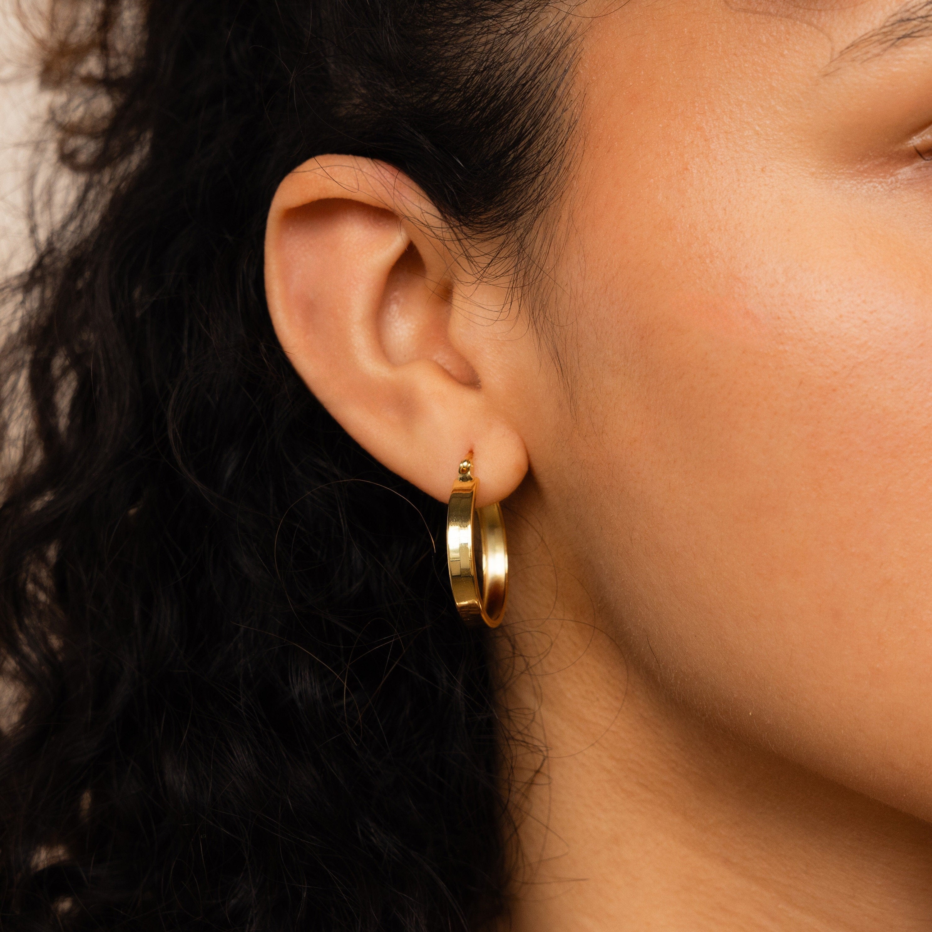 Close-up of a person with curly hair wearing Thick Hoops, shiny gold chunky earrings.