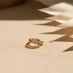 The Inside Out Huggies Set features gold hoop earrings with small clear gemstones that sparkle on a beige surface in soft, natural light, adding a subtle and refined touch to any look.