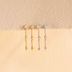 The Opal Chain Drop Earrings set includes four elegant pieces—two gold and two silver with opal-like stones—displayed on a textured surface. Perfect for bridesmaids seeking a refined, delicate touch.