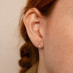 A woman’s ear is adorned with Opal & Diamond Marquise Studs, her braided hair softly framing these delicate earrings—an ideal bridesmaid gift.