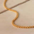 Diamond Bezel Tennis Necklace with round diamonds displayed on a beige stone surface—a stunning bridal necklace and a sophisticated gift for the bride.