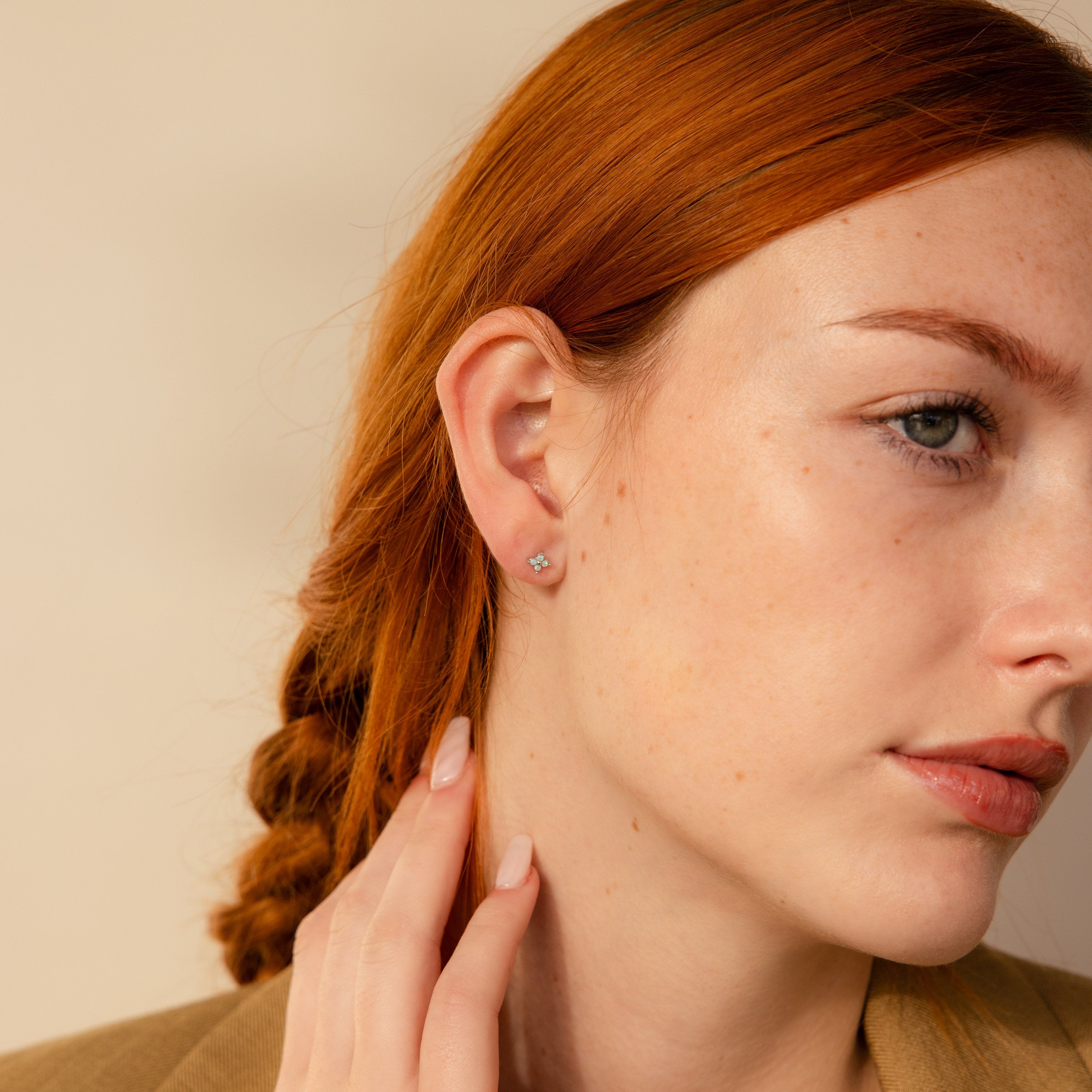 Close-up of a woman with red hair touching her neck, showcasing Opal Ivy Flower Studs—a meaningful gift that adds a subtle sparkle to her look.