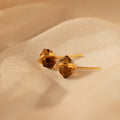 Herkimer Smoky Quartz Studs in gold and brown tones rest elegantly on soft, beige fabric.