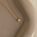 The Hexagon Diamond Necklace features a gold chain with a single rose-cut diamond pendant, showcased on a smooth beige ceramic dish.